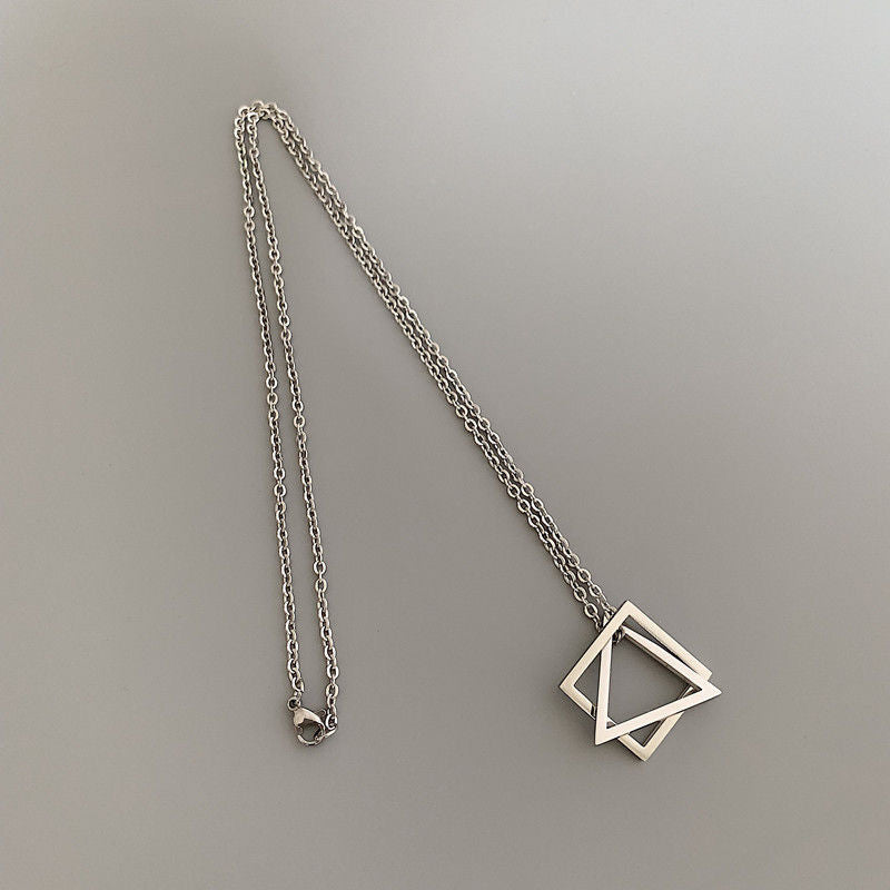 Minimalist silver necklace with interlocking square and triangle charms, laid flat on a light grey surface