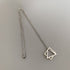 Minimalist silver necklace with interlocking square and triangle charms, laid flat on a light grey surface