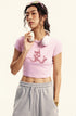 Pink cropped t-shirt with a pink devil girl and snake graphic, styled with gray sweatpants and white headphones