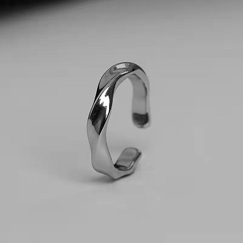 A silver twisted open ring standing upright on a gray surface, displaying its adjustable design with polished metal finish in a professional product shot