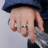 A model is wearing a silver twisted band ring on their finger while holding a crystal glass, showcasing minimalist jewelry styled with denim and dark clothing