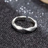 A silver geometric open ring displayed on a sparkly black surface, featuring a modern faceted design with polished finish that catches the light