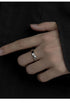 A model is wearing a silver twisted band ring on their finger against a black fabric background, showing the sleek minimalist jewelry design in low light