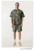 Model in olive t-shirt and shorts set with silver necklace, white socks and beige sneakers on cream background