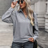 Woman wearing gray textured collared pullover with gold button details, paired with jeans and sunglasses against urban backdrop