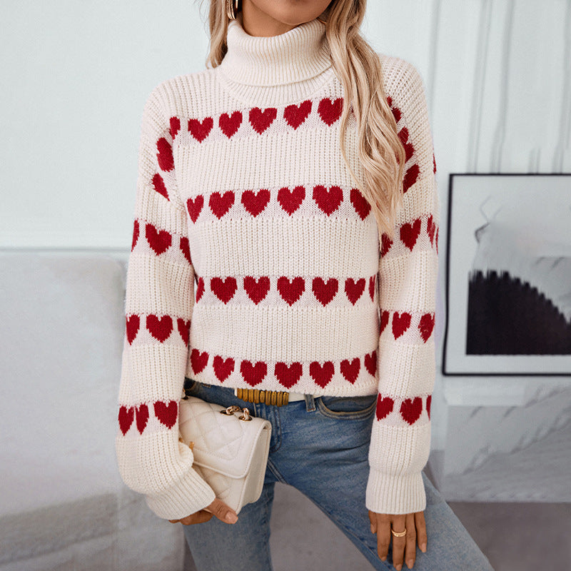 A woman wearing cream turtleneck sweater with red heart pattern stripes paired with blue jeans and cream handbag against white wall background