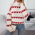 A woman wearing white knit turtleneck with horizontal red heart pattern rows, touching her neck while holding small quilted purse with blue jeans