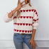 A woman wearing ivory turtleneck sweater with red heart stripe pattern holding phone while displaying gold bracelets and blue jeans
