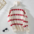 White chunky knit turtleneck sweater with horizontal red heart pattern rows displayed on white background with decorative gold element