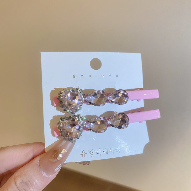 Pink alligator hair clips with faceted heart-shaped crystals and rhinestone trim, displayed on a white card.