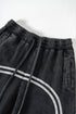 Close-up of elastic waistband with drawstring on black washed denim track pants featuring double gray side stripe detail