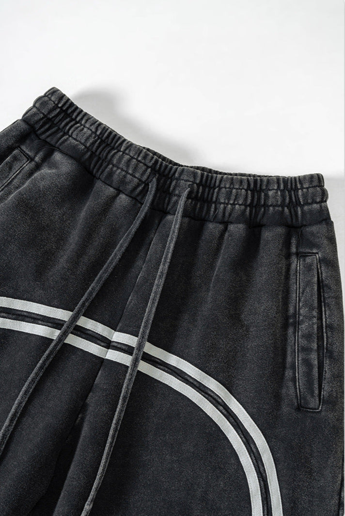 Close-up of elastic waistband with drawstring on black washed denim track pants featuring double gray side stripe detail
