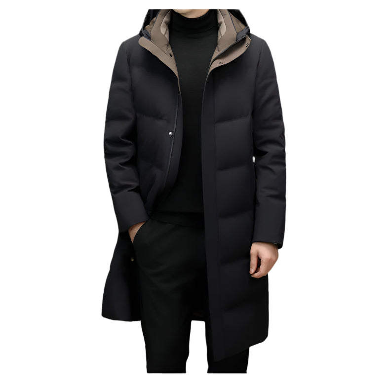 A man wearing a black long down coat with a hood, layered over a black turtleneck and pants, standing against a plain background