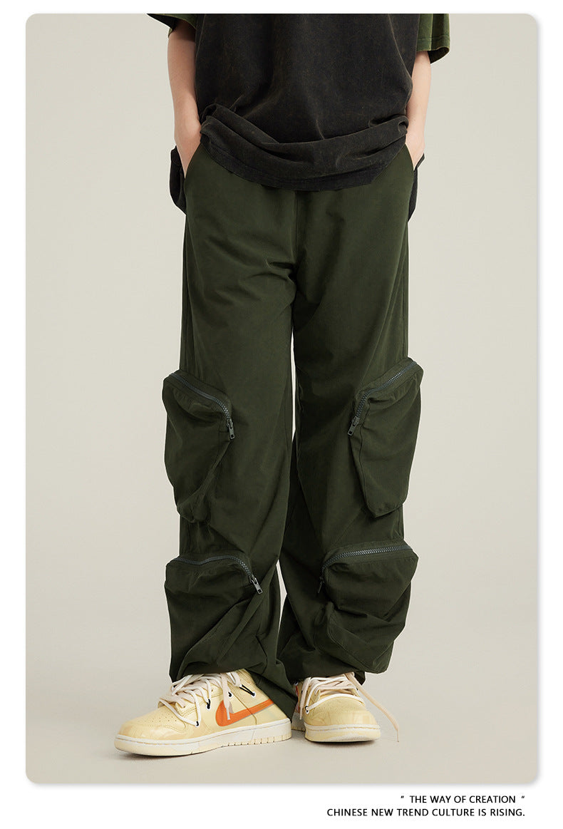 Close-up of olive green cargo pants with attached zippered utility pockets shown with black oversized top and cream sneakers