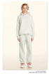 Model wearing light gray hoodie and sweatpants with silver headphones and red-accented white sneakers