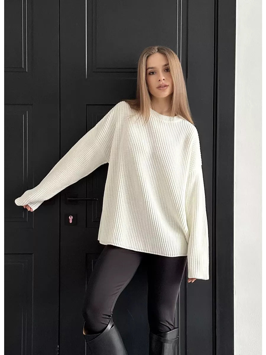 Cream colored ribbed knit sweater with relaxed fit and dropped shoulders, paired with black leggings against black paneled door