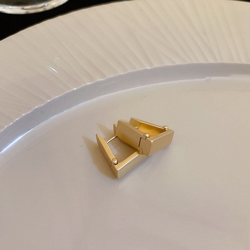 Square Gold Huggie Earrings – Minimalist gold huggie earrings with a geometric square shape, displayed on a white plate