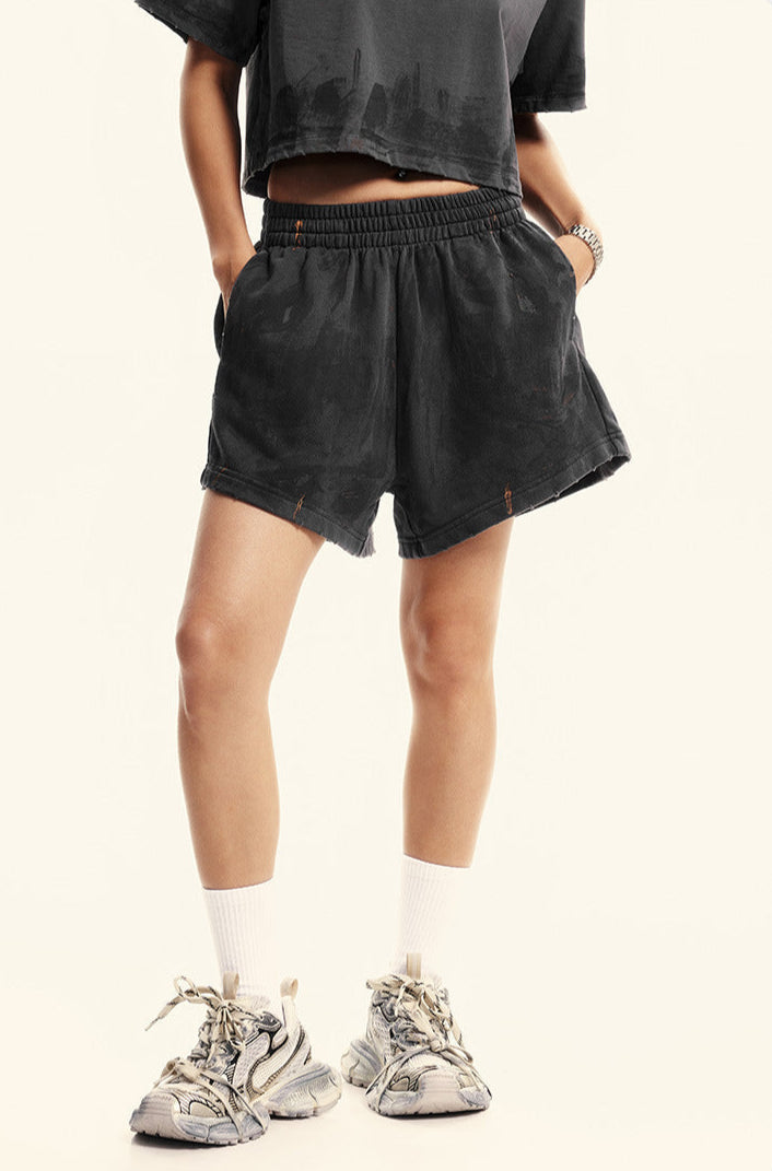 A woman in dark gray shorts with elastic waistband, white socks, and chunky white sneakers standing against white background