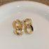 Gold interlocking chain link stud earrings on white surface