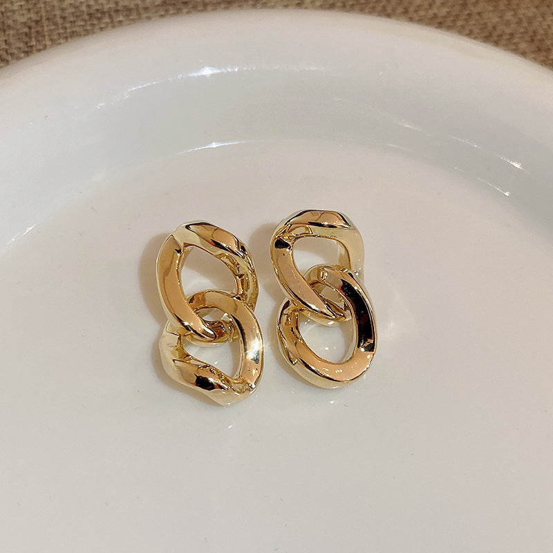 Gold interlocking chain link stud earrings on white surface