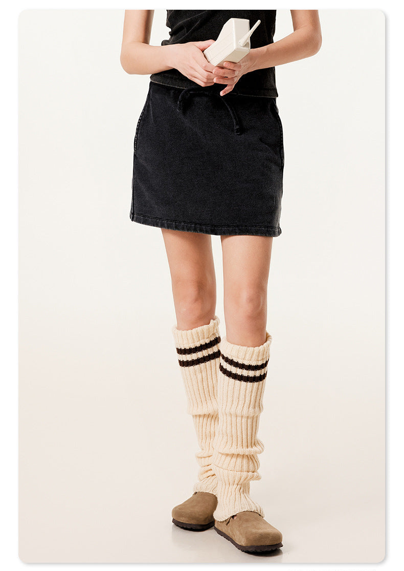 Model wearing black mini skirt with cream striped leg warmers, displaying casual styling with vintage phone prop