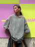 Person wearing a gray oversized sweatshirt against a colorful geometric background