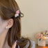 A woman with brown hair wears a small black claw clip adorned with pink and white heart-shaped embellishments, securing a side section of her hair.