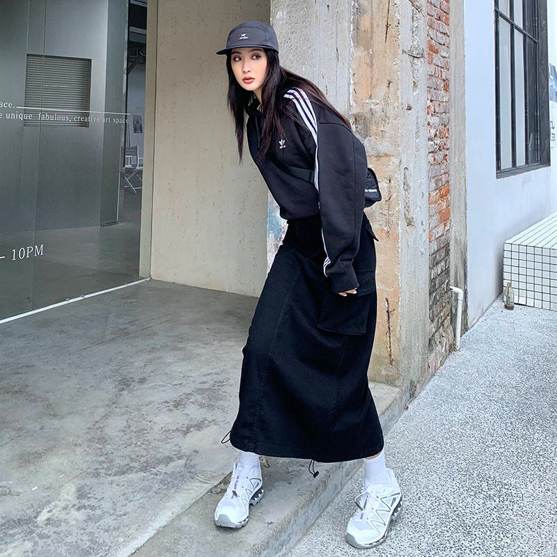 Side view of black maxi cargo skirt showing drawstring hem detail, paired with sporty streetwear accessories