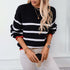 Trendy winter outfit featuring black and white striped knit sweater, layered gold necklaces, and white denim pants, holding coffee cup