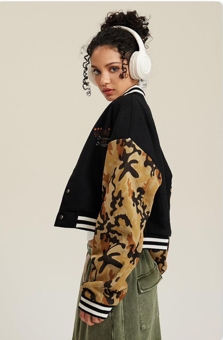 Side profile of black varsity jacket with tan camouflage sleeves, showing embroidered logo and cropped design