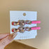 Pink alligator clips with teardrop and heart-shaped crystals, set in a rhinestone frame, displayed on a card.