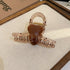 A translucent brown acrylic hair clip featuring a glossy brown heart in the center, placed on a beige fabric surface.