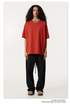 Female model in bright red oversized t-shirt with relaxed crew neck, paired with black drawstring pants and beige shoes, minimal styling