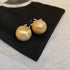 Gold Satin-Finish Stud Earrings – Round gold stud earrings with a smooth satin texture, placed on a black fabric pouch