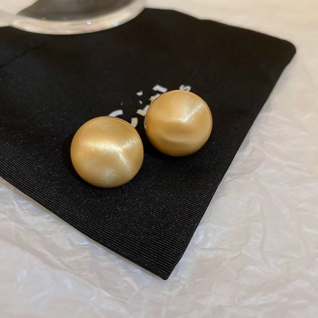 Gold Satin-Finish Stud Earrings – Round gold stud earrings with a smooth satin texture, placed on a black fabric pouch