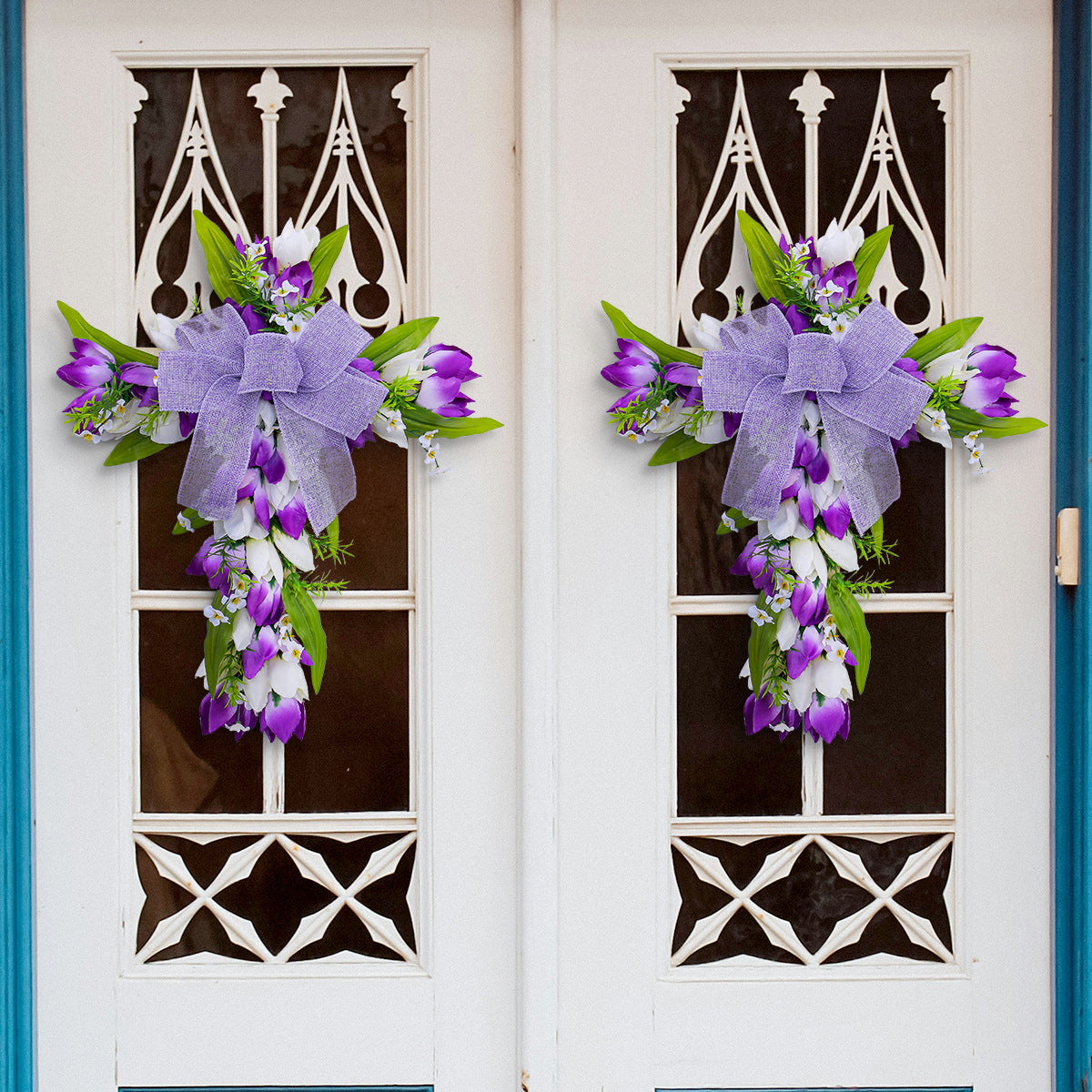 Two purple floral cross wreaths with bows on white double doors, featuring tulips, greenery, and a cascading floral design.