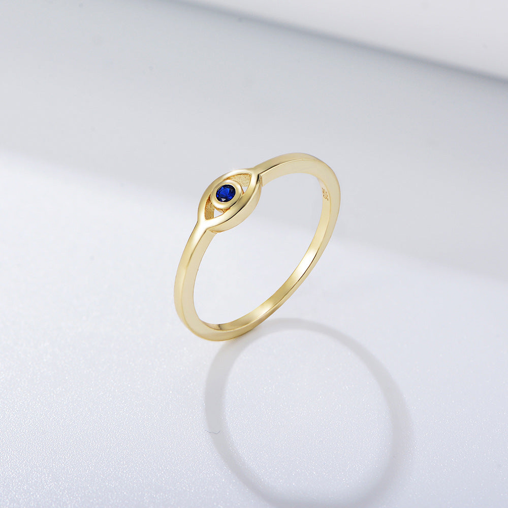 Gold ring with small blue sapphire in eye-shaped setting against white background