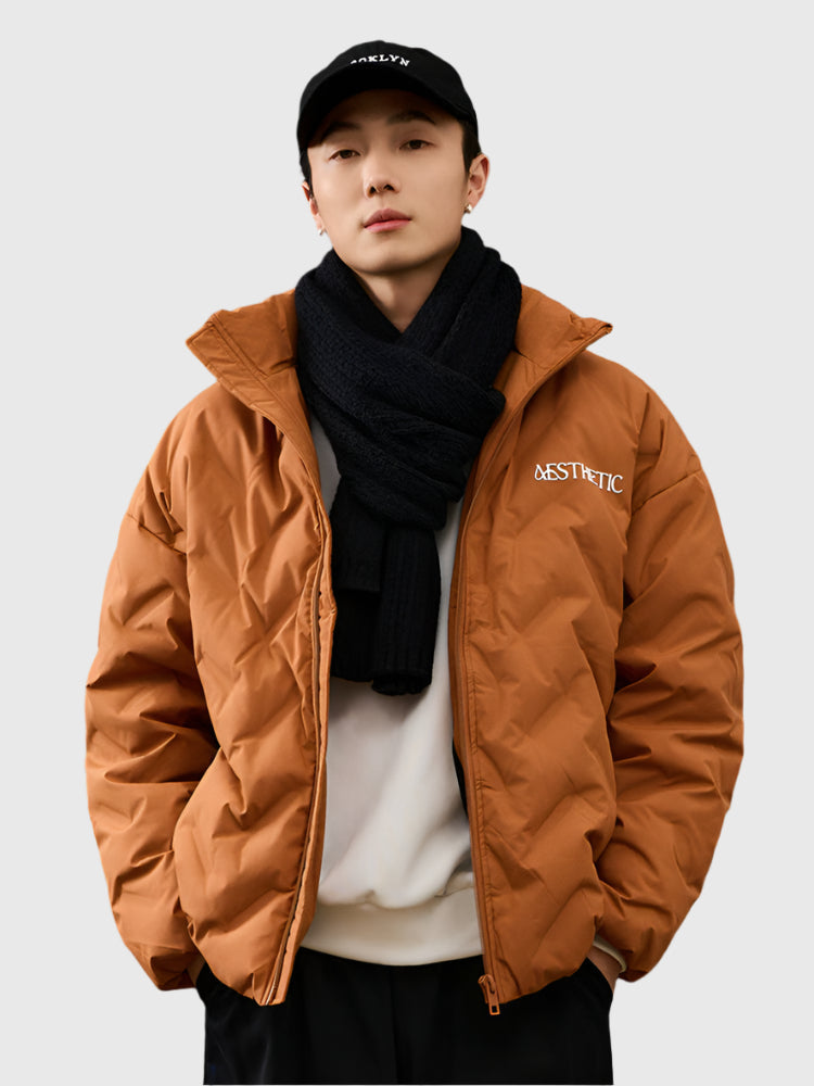 Young man wearing camel brown Aesthetic quilted puffer jacket styled with black scarf and Brooklyn baseball cap against white backdrop