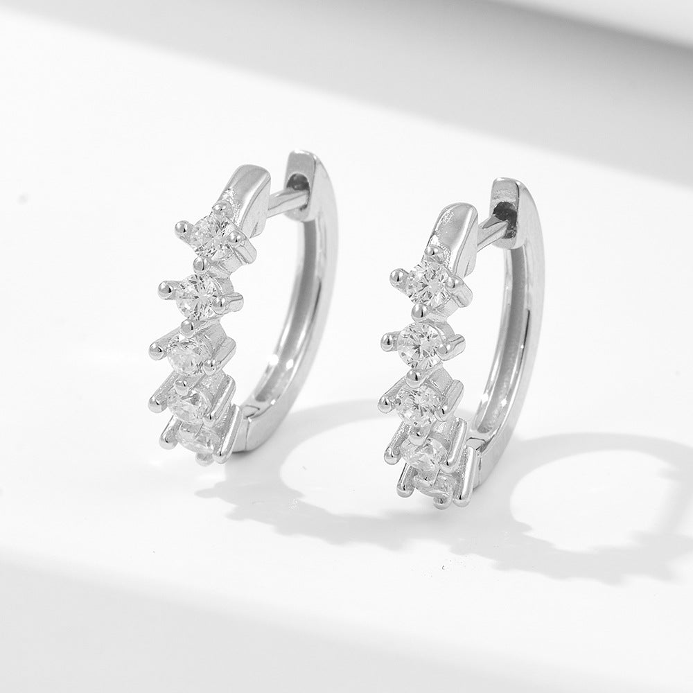Sterling silver huggie hoop earrings with five graduated crystal stones on white background