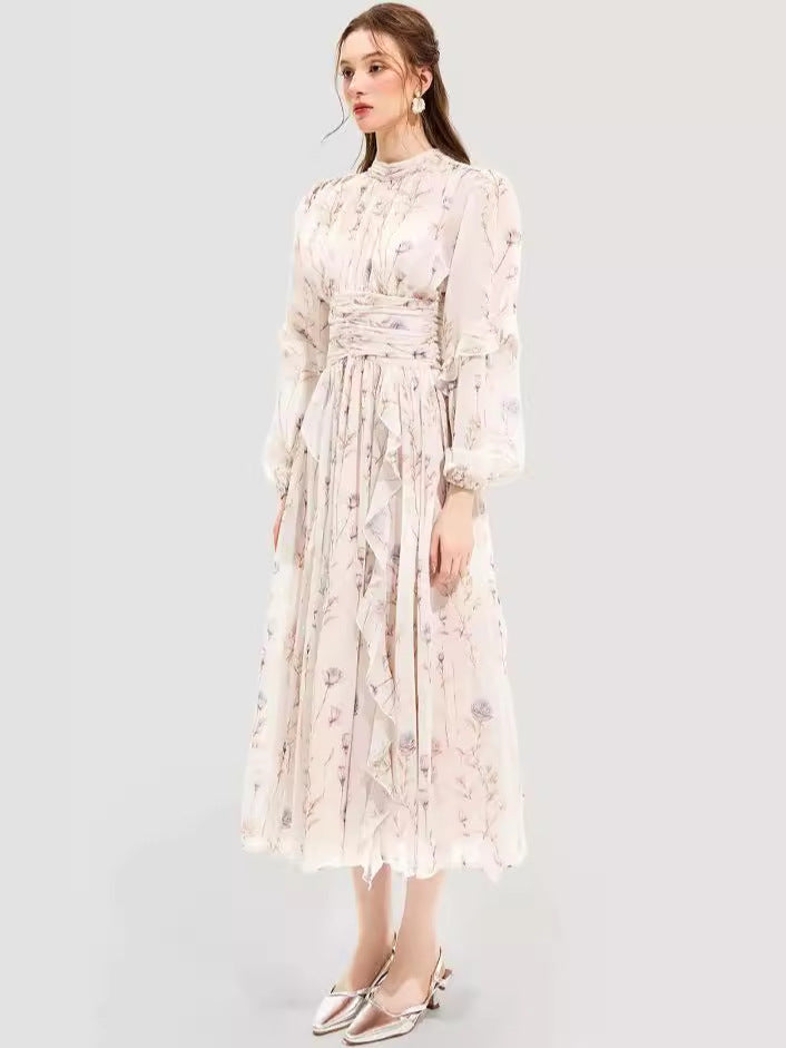 Side view of a woman in a long-sleeve floral maxi dress with a high neckline, ruched waist, and flowing ruffled skirt, styled with statement earrings