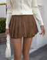 Woman wearing a brown pleated mini skort with a white cable knit sweater, accessorized with a white ruched handbag.