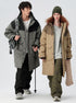 A man and woman wearing coordinating technical parkas stand against white background - his in gray/black with backpack, hers in beige/olive