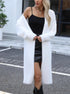 A woman wearing a white fuzzy cardigan over a black mini dress and knee-high boots, accessorized with a silver necklace