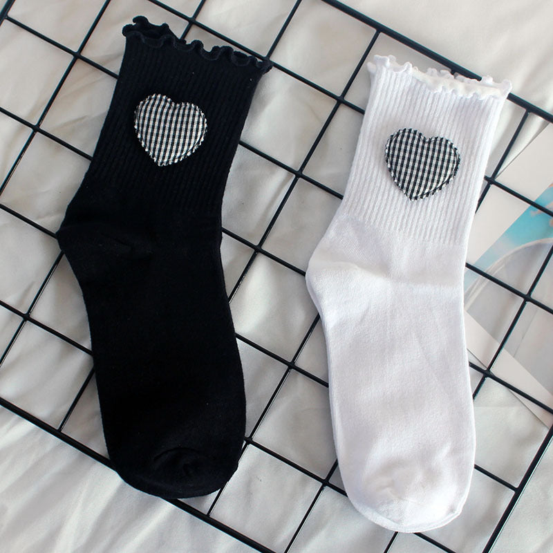 Ribbed crew socks in black and white with gingham heart patches, displayed on a grid surface
