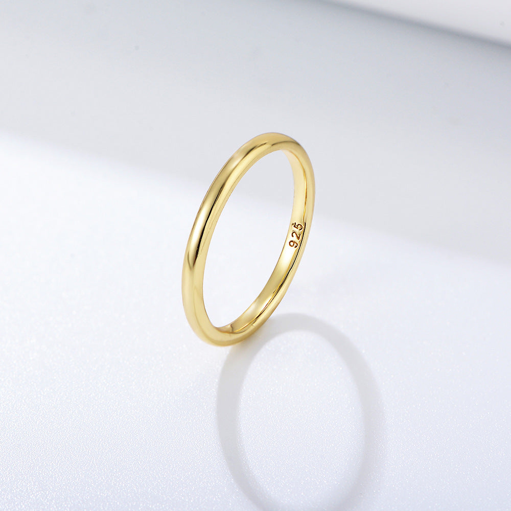 A gold thin stackable band ring with 925 stamp displayed on white surface casting subtle shadow