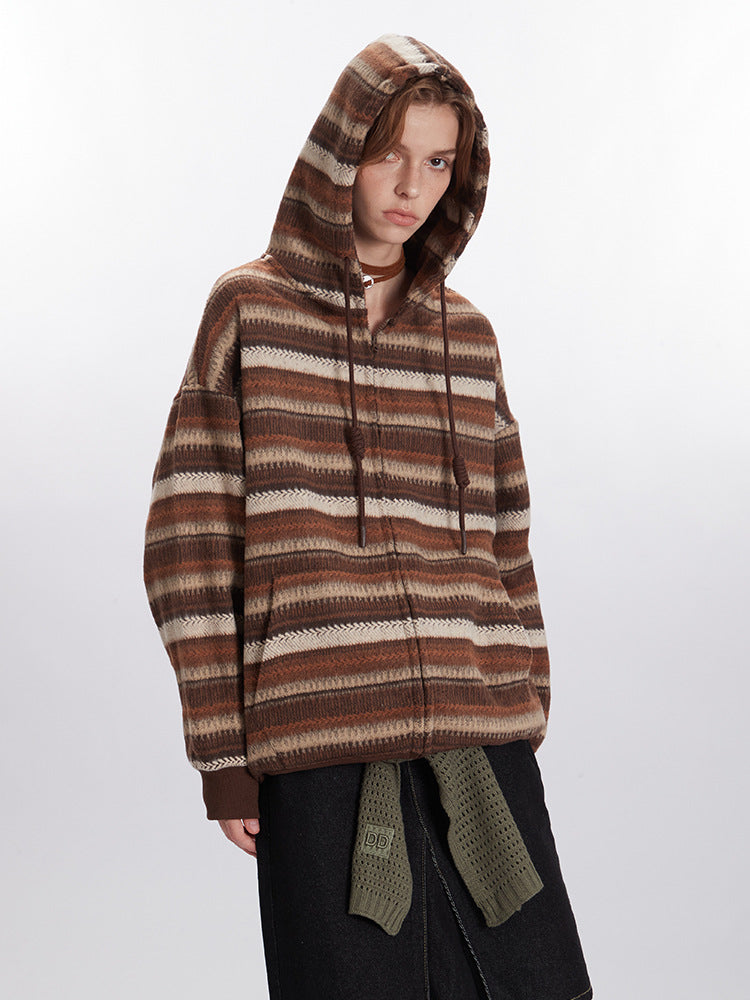 Woman with hood up modeling brown striped zip hoodie with chevron pattern detail, paired with black denim skirt and olive green accent belt
