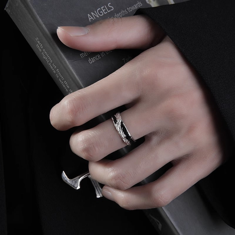 Close-up of a hand wearing a textured silver ring while holding a black book, with a dark background.