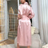 Back view of a woman in pink silk robe showing long sleeves and tie waist, standing in an elegant room