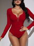 Front view of a woman in a red ribbed bodysuit with a deep V-neck zipper, wearing silver hoop earrings and sunglasses, posing against a white wall.