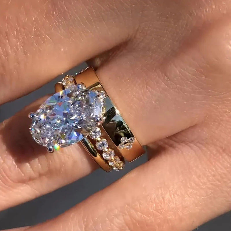 A woman wearing gold engagement ring and diamond wedding band set, close-up showing sparkle of oval center stone on finger